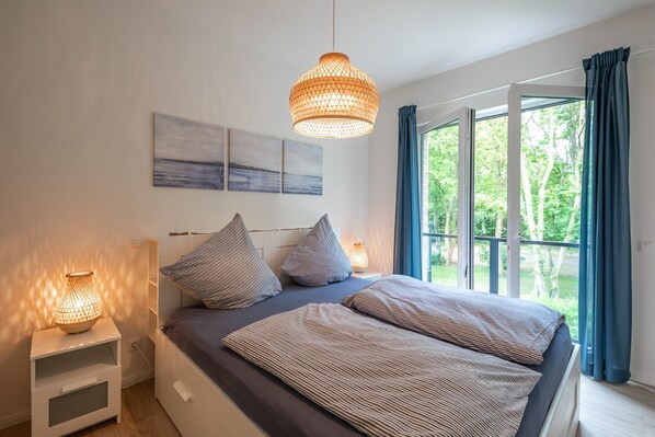Ein Schlafzimmer mit einem großen Bett, zwei Nachttischlampen und Blick auf Grün hinter dem Fenster.