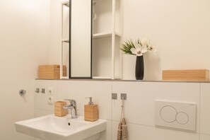 Ein Badezimmer mit einem weißen Waschbecken, einem Spiegel und einer Wandvase mit weißen Blumen.