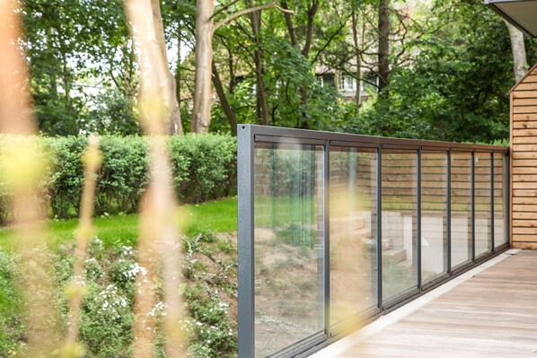 Eine Holzterrasse mit Glasgeländer, das auf einen Garten blickt.