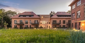 A modern building with a brick facade, multiple balconies, and a well-maintained garden area.
