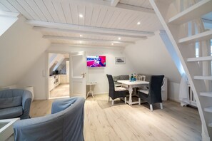A modern loft apartment with a dining area, a living room with a sofa, and a kitchen in the background. - Vacation apartment Silbermöwe- Herrenhof Wrixum - Vacation in the historic (Wyk auf Föhr)