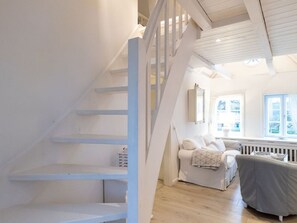 A staircase with white railings leading to a room with a white sofa and a window with blinds. - Vacation apartment Silbermöwe- Herrenhof Wrixum - Vacation in the historic (Wyk auf Föhr)