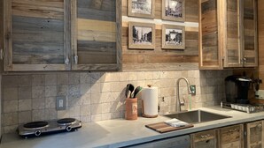 Una cocina con armarios de madera, salpicadero azulejado, un lavabo, una cafetera y una balanza.