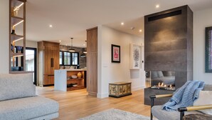 Ein modernes Wohnzimmer mit Kamin, einer Couch, einem Couchtisch und einer Küche im Hintergrund.
