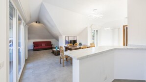 Amplia sala de estar con una mesa de comedor, un sofá rojo y una zona de cocina con mostrador y sillas.