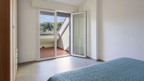 Un dormitorio con cama, puerta corrediza al balcón y vista a zonas verdes.