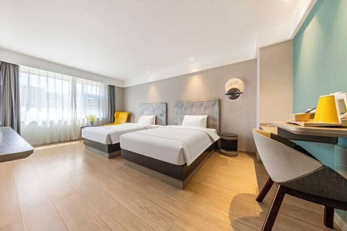 A hotel room with two beds, a desk, a chair, a lamp, and a trash bin.