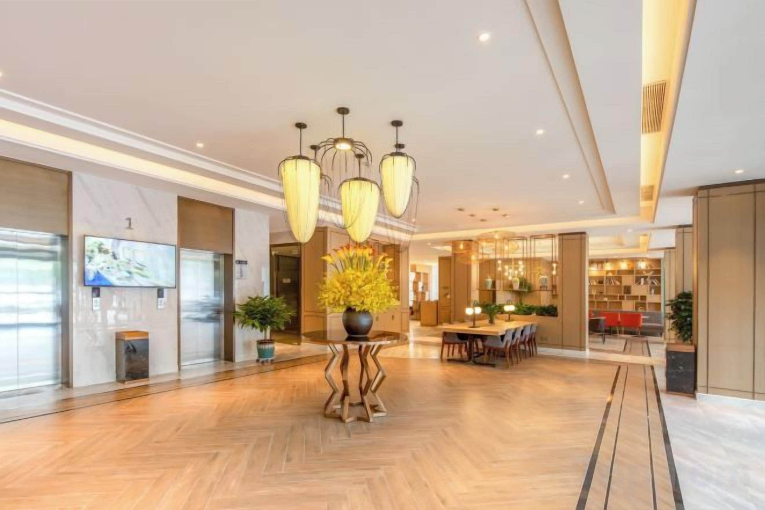 A spacious lobby with a herringbone floor, a central plant arrangement, and a modern chandelier.