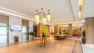 A spacious lobby with a herringbone floor, a central plant arrangement, and a modern chandelier.