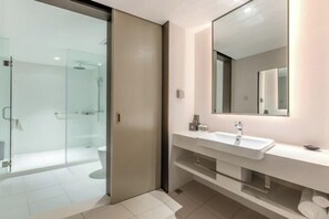 Un baño moderno con cabina de ducha de vidrio, un lavamanos blanco con espejo y un perchero para toallas.