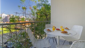 Ein Balkon mit weißen Korbmöbeln, einem Tisch mit Croissants und einem Glas Orangensaft.