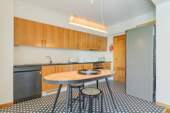 A compact kitchen with wooden cabinets, a modern light fixture, a built-in dishwasher, and a patterned floor. - Elena Apartment by Atlantic Holiday (Funchal)