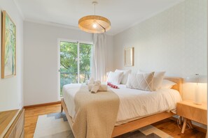 A bedroom with a large bed, a bedside table with a lamp, a window with curtains, and a view of trees outside. - Elena Apartment by Atlantic Holiday (Funchal)