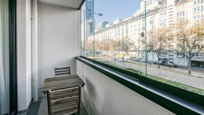 Ein Balkon mit Tisch und Stühlen, der auf eine Straße mit Gebäuden und Bäumen blickt.