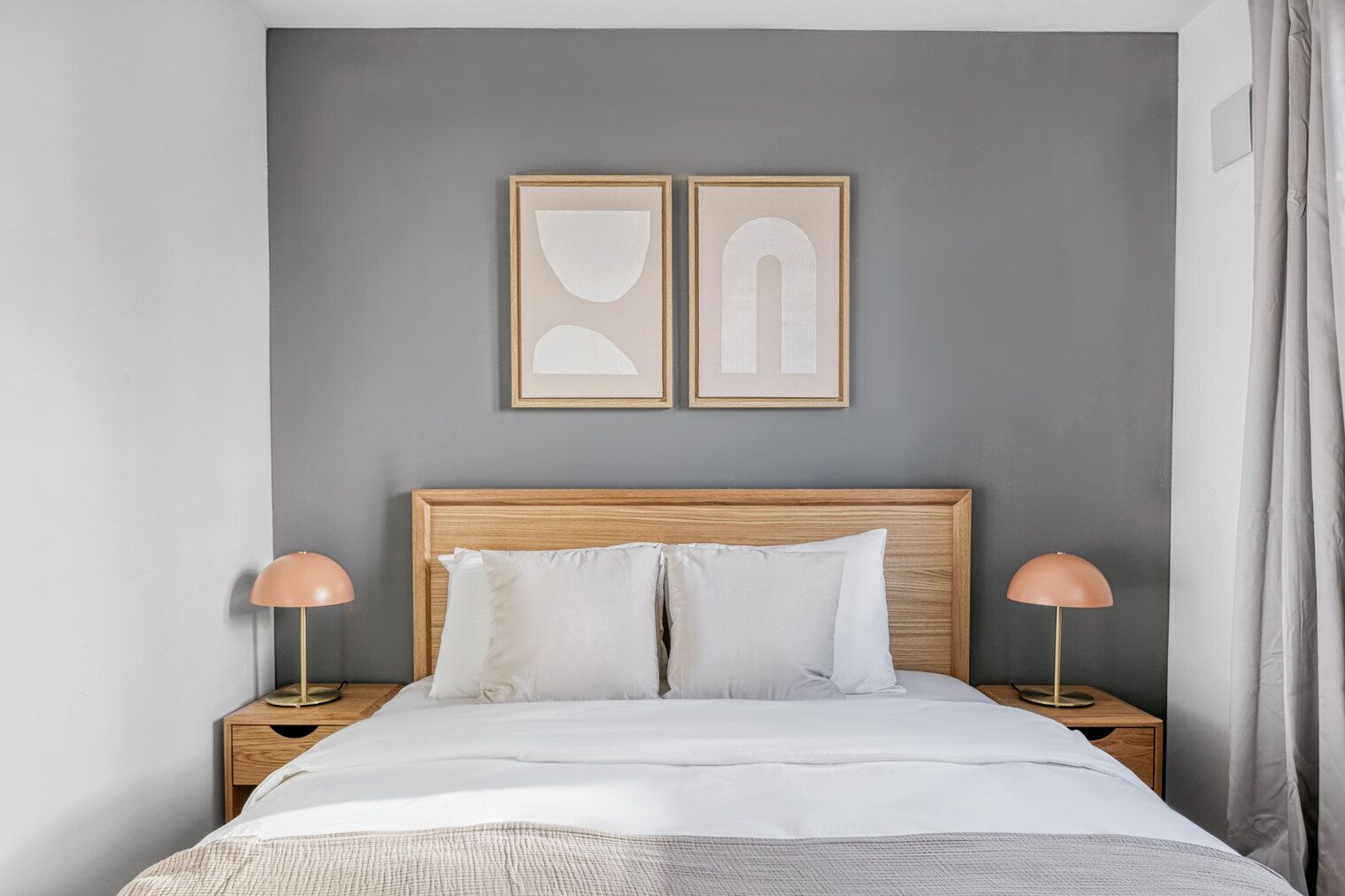 Un dormitorio con cabecera de madera, dos lámparas de noche, una cama con ropa de cama blanca y dos obras de arte enmarcadas en la pared.