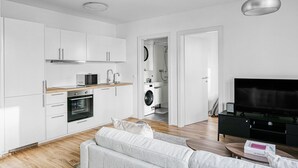 Eine moderne Küche mit weißen Schränken, einer Mikrowelle, einem Backofen und einer Waschmaschine im Hintergrund.