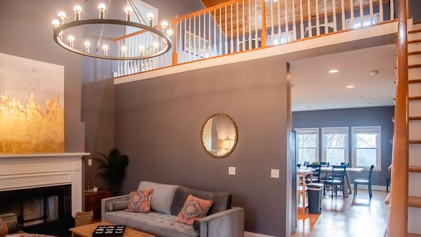 Una sala de estar amplia con un sofá gris, una chimenea y un comedor al fondo.