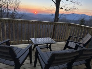 Une terrasse avec une table et des chaises, offrant une vue sur un paysage montagneux au coucher du soleil.