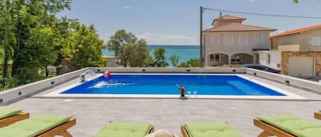 A pool with lounge chairs and a view of the sea.