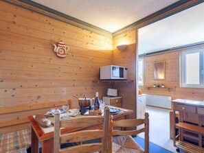 Interior de una cabaña de madera con una mesa de comedor, sillas, un microondas y una pequeña cocina.