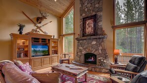 Un salon chaleureux avec une cheminée en pierre, des meubles en bois et une grande fenêtre donnant sur une forêt.
