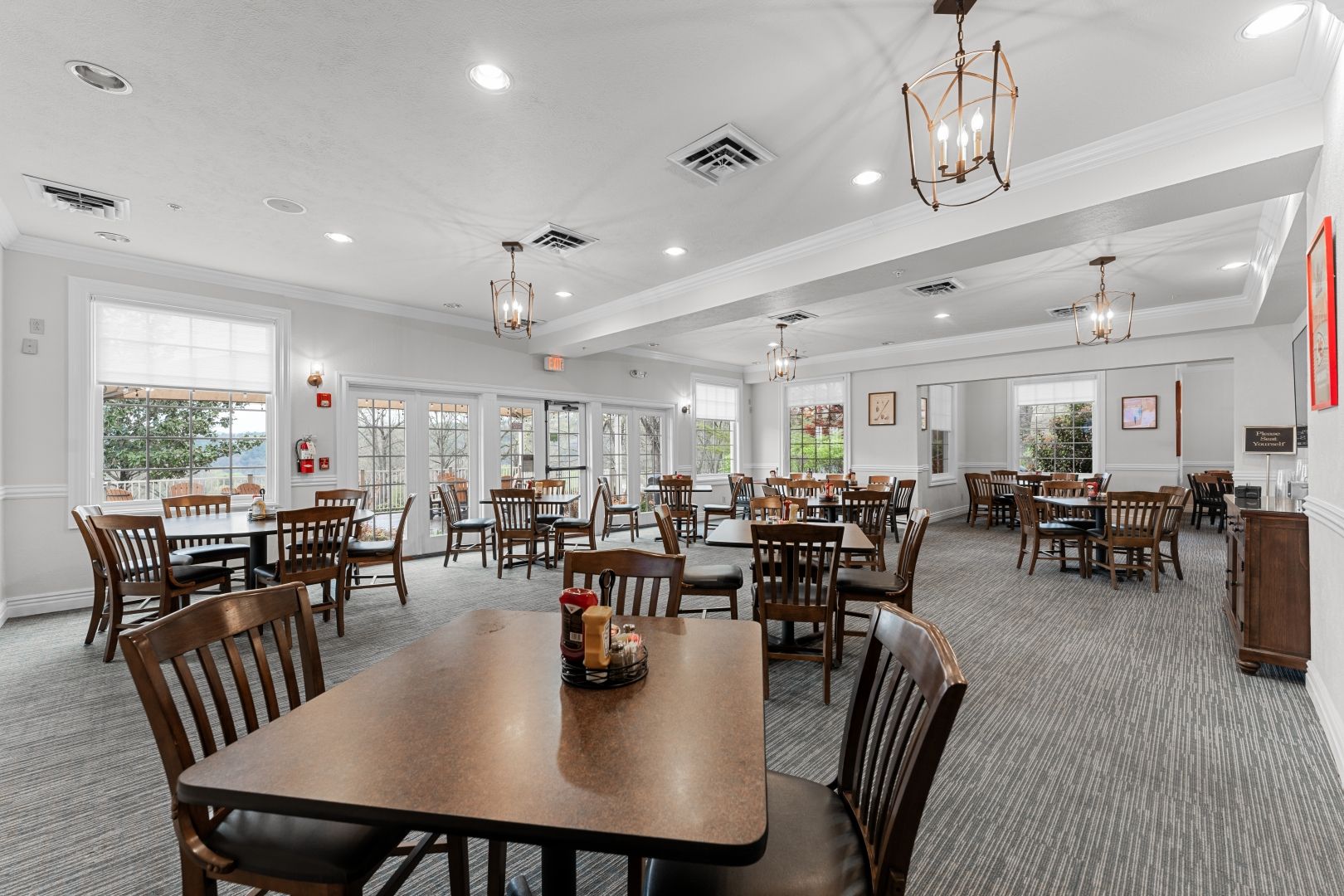 A spacious dining area with multiple tables and chairs, large windows, and ceiling lights.