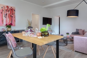 Ein modernes Wohnzimmer mit einem Holzesstisch, der für eine Mahlzeit gedeckt ist, einer Couch und einem an der Wand montierten Fernseher.