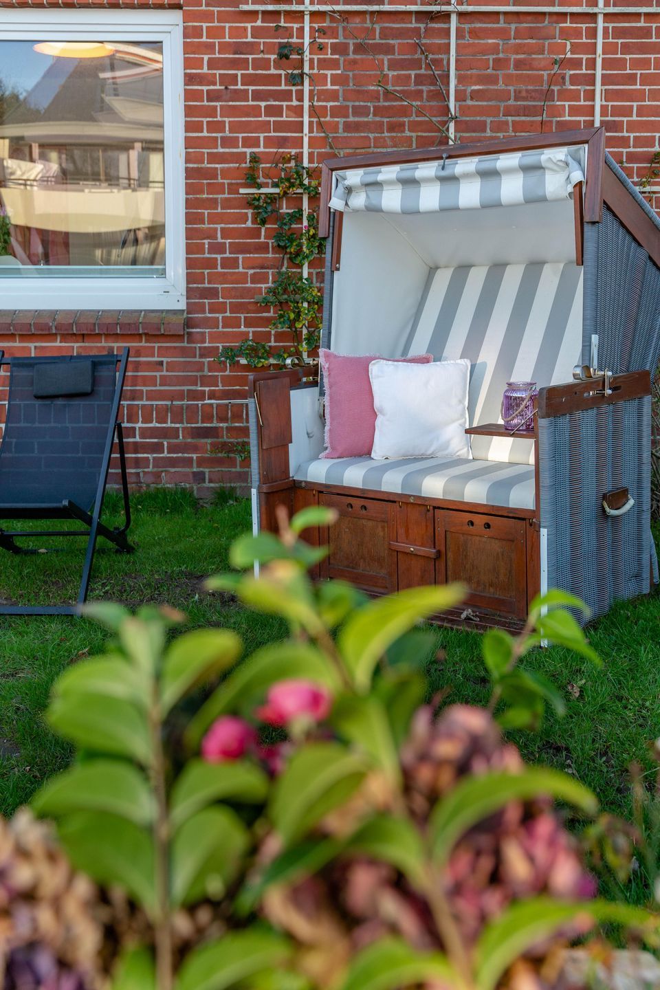 Ein Sitzbereich im Garten mit einer gestreiften gepolsterten Bank, einem kleinen Tisch und einem Stuhl.