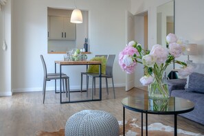 Un salon moderne comprenant un coin repas, un canapé, une table basse en verre et un vase de fleurs.