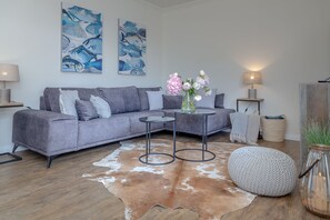 Un salon moderne avec un canapé gris, une table basse ronde, un tapis en peau de vache et deux tableaux accrochés au mur.