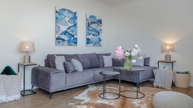A modern living room with a grey sofa, two side tables with lamps, a round coffee table, a vase with flowers, and a cowhide rug. - Königsmann - Close to the beach and centrally located, modern vacation apartment with (Sylt)