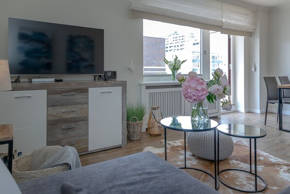 Een moderne woonkamer met een flatscreen televisie, een eethoek met een tafel en stoelen, en een groot raam met uitzicht op de stad.