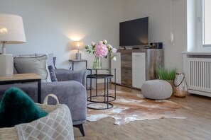 Een moderne woonkamer met een bank, een salontafel, een lamp, een televisie en een kleden van koeienhuid.