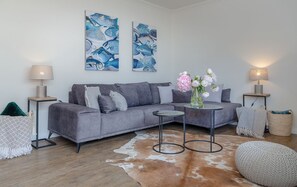 A modern living room with a grey sofa, two side tables with lamps, a round coffee table, a vase with flowers, and a cowhide rug. - Königsmann - Close to the beach and centrally located, modern vacation apartment with (Sylt)