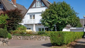 A two-story house with a sloped roof, a stone wall in front, and a well-maintained garden.