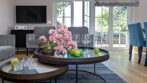 A modern living room with two round tables, one with a flower vase and green apples, and the other with wine glasses and a bowl.