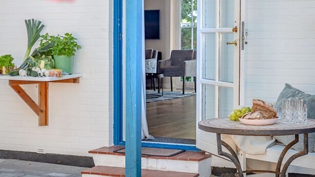 An outdoor seating area with a table and chairs, a small garden with plants, and a door leading to an interior space.