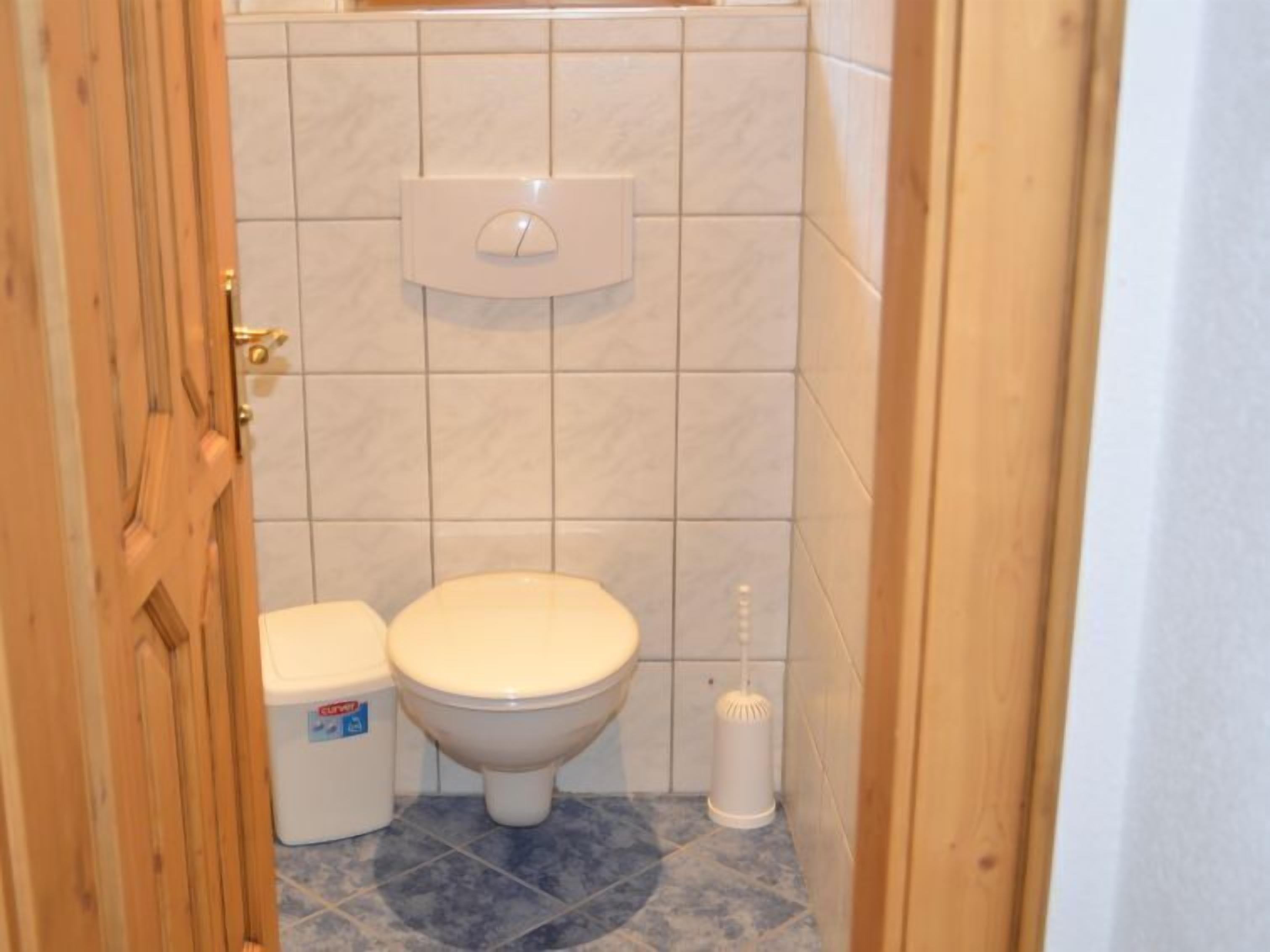 A small bathroom with a toilet, a trash bin, and a toilet brush.