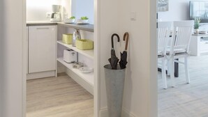Ett modernt kök med vita skåp, en kaffebryggare och ett litet kylskåp. På golvet står en grå metallbehållare med paraplyer i.