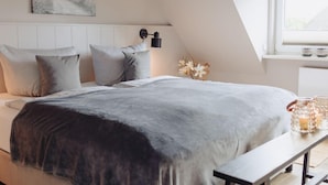 Et soveværelse med seng, puder, et natbord, en lampe, et vindue og et billede på væggen.