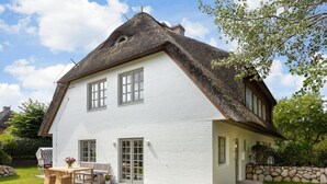 A two-story house with a white exterior, a thatched roof, and a small patio with a table and chairs. - Tortuga - Spacious vacation home in the dreamlike captain's village of Keitum (Sylt-Ost)
