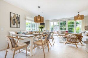 A spacious dining area with a wooden table and chairs, large windows with a view of greenery, and a modern pendant light fixture. - Tortuga - Spacious vacation home in the dreamlike captain's village of Keitum (Sylt-Ost)