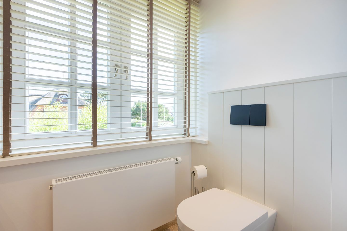 A bathroom with a toilet, a radiator, and a window with blinds.