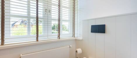 A bathroom with a toilet, a radiator, and a window with blinds.