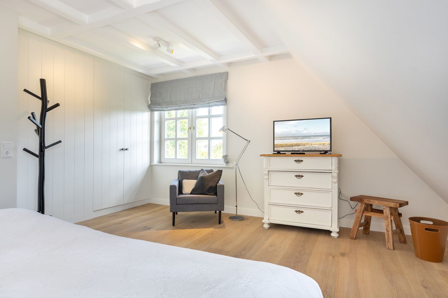 A bedroom with a bed, a dresser, a chair, a TV, a window, and a coat rack.