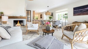 A spacious living room with a fireplace, wicker furniture, and a dining area with natural light. - Tortuga - Spacious vacation home in the dreamlike captain's village of Keitum (Sylt-Ost)