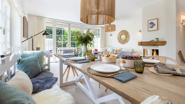 A spacious living room with a wooden dining table, a fireplace, and a large window overlooking a garden. - Tortuga - Spacious vacation home in the dreamlike captain's village of Keitum (Sylt-Ost)