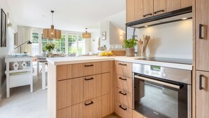 A modern kitchen with wooden cabinets, a built-in oven, and a dining area with a white table and chairs. - Tortuga - Spacious vacation home in the dreamlike captain's village of Keitum (Sylt-Ost)