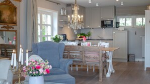 A spacious living room with a large grey armchair, a wooden dining table, and a chandelier.