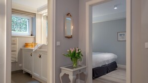 A bedroom with a bed, a bedside table with a vase of flowers, a dresser, and a window with blinds.